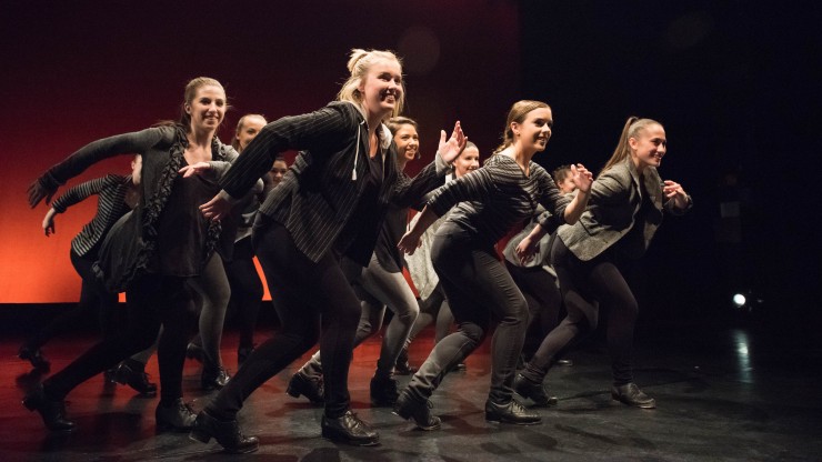 A group of dance students smiling while onstage during a tap dance performance. 