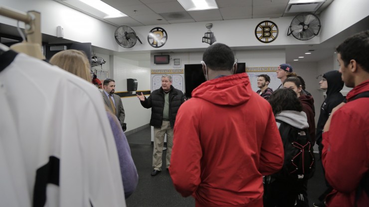 A professor speaking to a group of students inside the Providence Bruins lockerroom while on a tour of the facility.