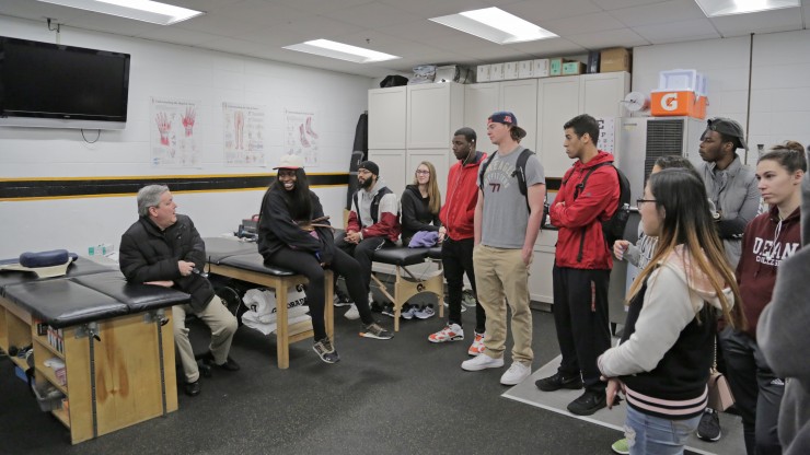 A professor explaining sports management to a group of students who are gathered around listening. 