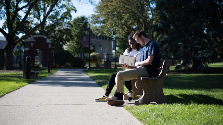 Students studying together on a bench outside of Awpie Way in front of Dean Hall.