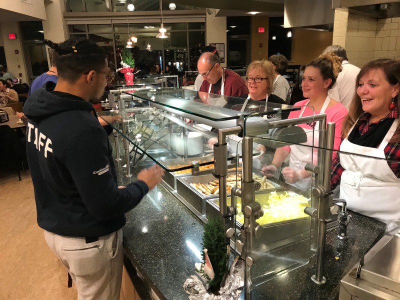 Image of a student being served breakfast food by faculty and staff at late night breakfast. 